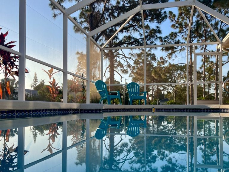 Blaues Wasser im Pool mit zwei Stühlen in einer überdachten Terrasse umgeben von Pflanzen.