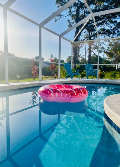 Rosa Schwimmring im Pool, umgeben von Sonnenschein und grüner Landschaft.